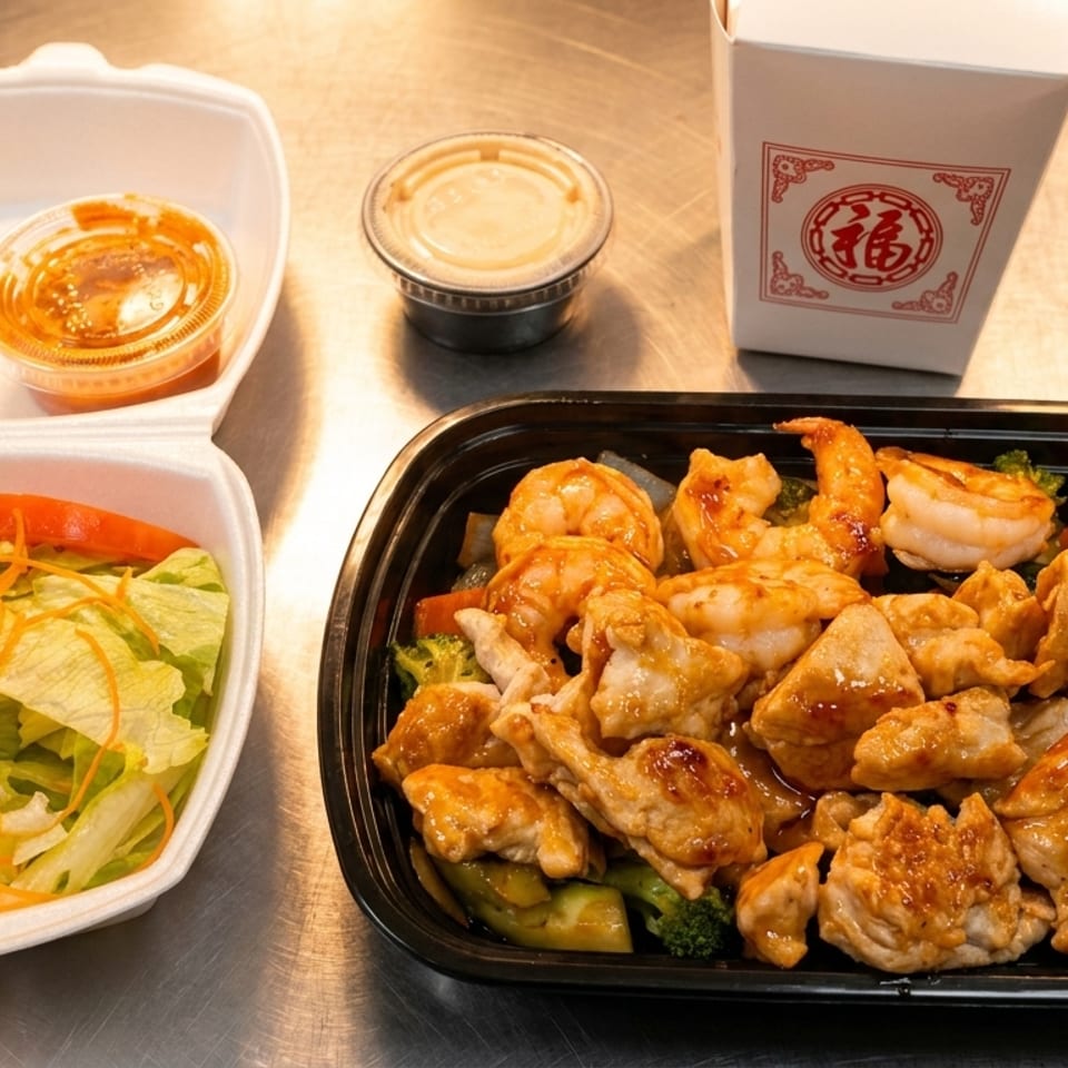 Chinese takeout meal with chicken and shrimp, a side salad, and sauces on a metal surface.